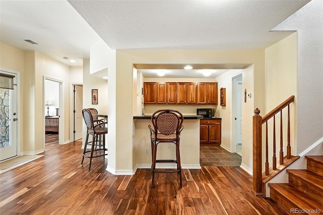 4944 W 107th Loop, Westminster, CO 80031 - kitchen with dark countertops, a kitchen breakfast bar, dark wood-style flooring, brown cabinets, and recessed lighting