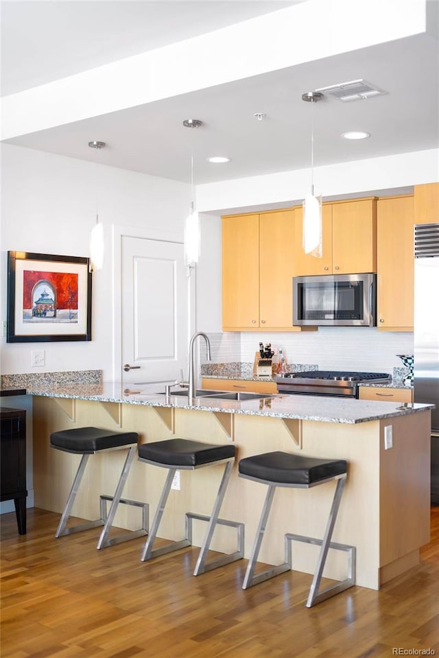 2001 Lincoln St Unit 1723, Denver, CO 80202 - kitchen featuring appliances with stainless steel finishes, wood finished floors, decorative backsplash, light stone countertops, and a breakfast bar