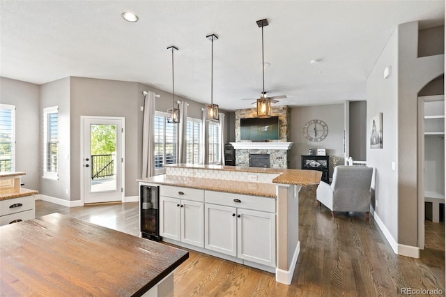 444 Pasada Way, Monument, CO 80132 - kitchen featuring wine cooler, a kitchen island, a fireplace, a ceiling fan, and wood finished floors