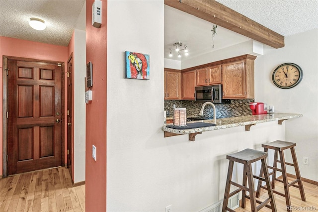 1950 S Helena St Unit D, Aurora, CO 80013 - kitchen featuring stainless steel microwave, a kitchen breakfast bar, beam ceiling, a textured ceiling, and backsplash