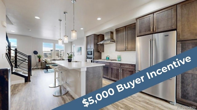 8742 E 47th Ave, Denver, CO 80238 - kitchen featuring wall chimney range hood, appliances with stainless steel finishes, light wood finished floors, dark brown cabinets, and recessed lighting