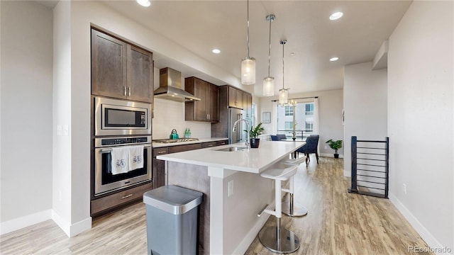 8742 E 47th Ave, Denver, CO 80238 - kitchen featuring stainless steel appliances, wall chimney range hood, an island with sink, light wood-style floors, and recessed lighting