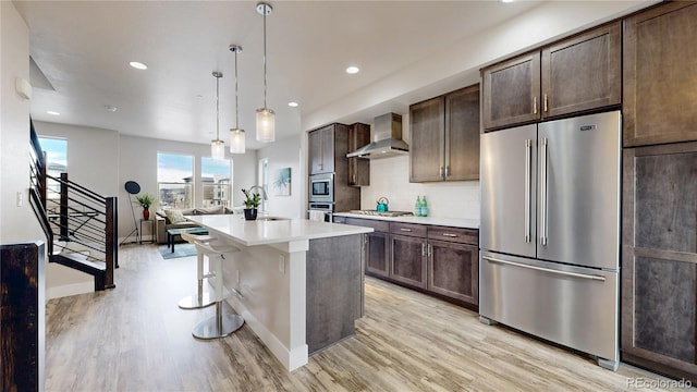 8742 E 47th Ave, Denver, CO 80238 - kitchen featuring stainless steel appliances, wall chimney exhaust hood, light wood-style floors, dark brown cabinets, and a sink