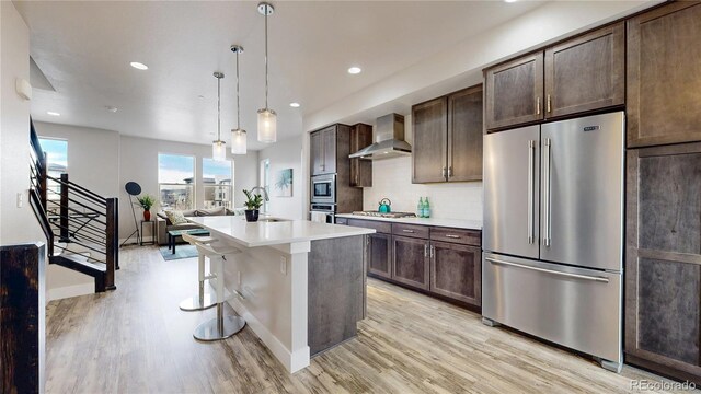 8742 E 47th Ave, Denver, CO 80238 - kitchen with appliances with stainless steel finishes, wall chimney range hood, light wood-type flooring, dark brown cabinetry, and light countertops