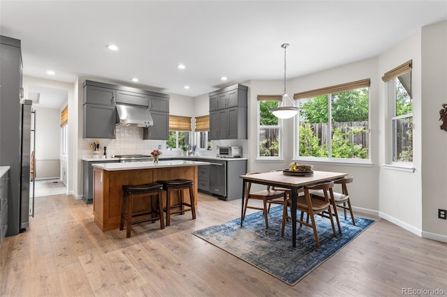 6643 Orion Ct, Arvada, CO 80007 - kitchen featuring wall chimney range hood, appliances with stainless steel finishes, gray cabinets, a center island, and light countertops