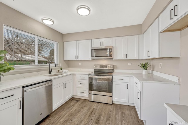 kitchen with white cabinets, stainless steel appliances, light hardwood / wood-style flooring, and sink