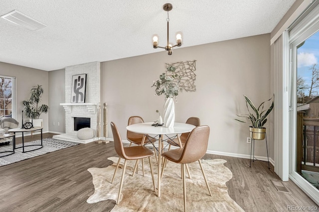 dining area with a notable chandelier, a large fireplace, wood-type flooring, and a textured ceiling