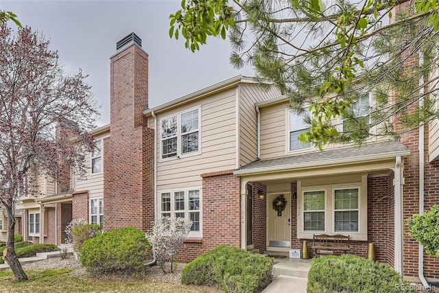view of property featuring a chimney, a porch, and brick siding