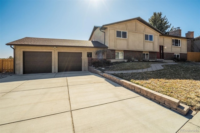 split level home with concrete driveway, an attached garage, fence, and brick siding