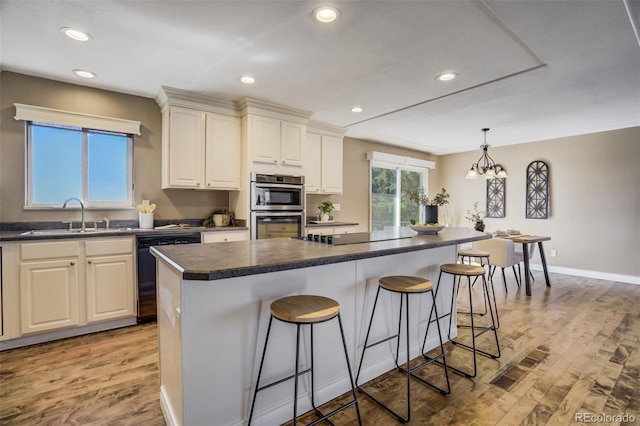 kitchen with dark countertops, a breakfast bar area, dishwashing machine, black electric cooktop, and a sink