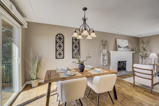 dining room with a notable chandelier, a fireplace, baseboards, and wood finished floors