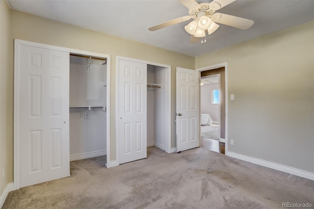 unfurnished bedroom with baseboards, two closets, ceiling fan, and carpet flooring