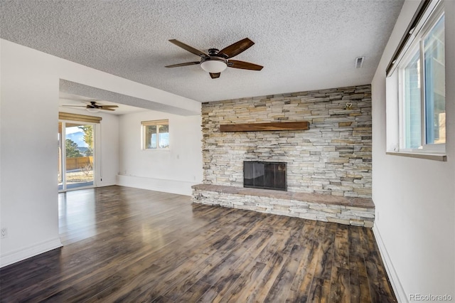 unfurnished living room with a stone fireplace, wood finished floors, and a textured ceiling