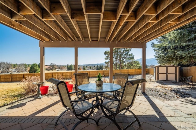 view of patio / terrace with a fenced backyard, an outdoor structure, outdoor dining space, a mountain view, and a storage unit