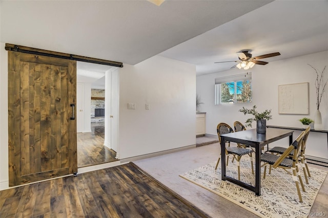 dining space with a barn door, wood finished floors, baseboards, and ceiling fan