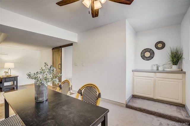 dining area with baseboards, light colored carpet, a ceiling fan, and a barn door