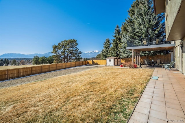 view of yard with a storage shed, a fenced backyard, an outdoor structure, a mountain view, and a patio