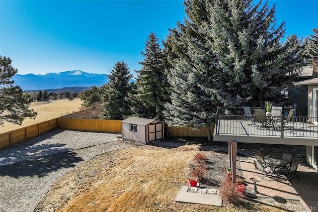 view of yard featuring outdoor dining area, a fenced backyard, an outdoor structure, a mountain view, and a storage unit