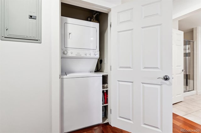 clothes washing area with electric panel, stacked washer / drying machine, and tile patterned floors