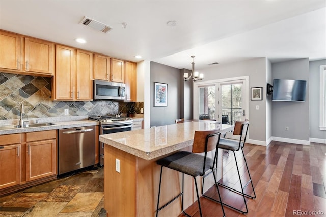 kitchen with stainless steel appliances, pendant lighting, a kitchen island, sink, and tasteful backsplash