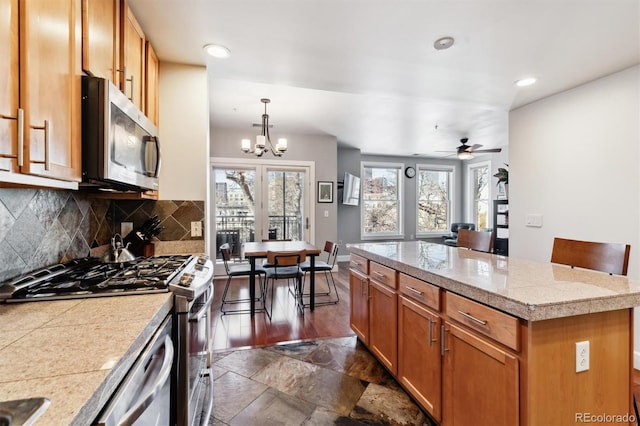 kitchen with decorative light fixtures, decorative backsplash, a kitchen island, ceiling fan with notable chandelier, and appliances with stainless steel finishes