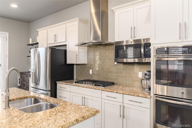 kitchen with white cabinetry, appliances with stainless steel finishes, sink, and wall chimney range hood