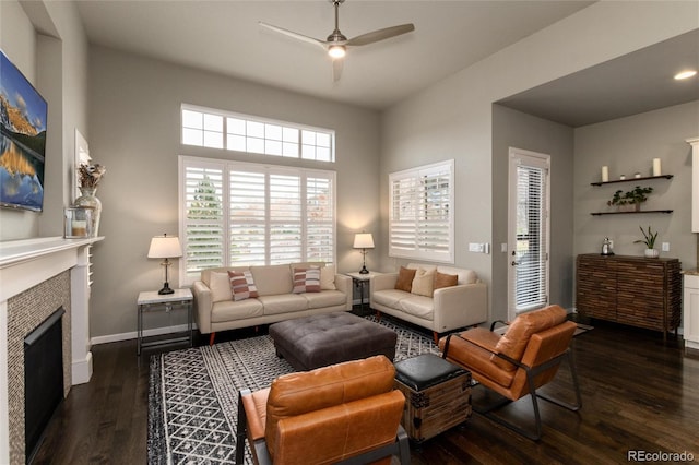 living room with a tiled fireplace, dark wood-type flooring, and ceiling fan