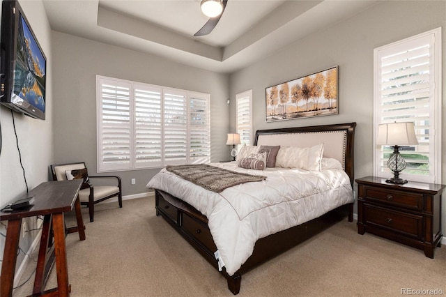 bedroom featuring ceiling fan, a tray ceiling, and light carpet