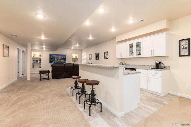 kitchen featuring a kitchen island with sink, a kitchen breakfast bar, light stone counters, white cabinets, and light carpet