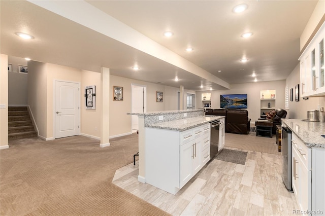 kitchen featuring a kitchen island, white cabinets, a kitchen breakfast bar, light colored carpet, and light stone countertops