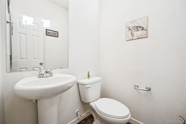 half bathroom with baseboards, a sink, and toilet