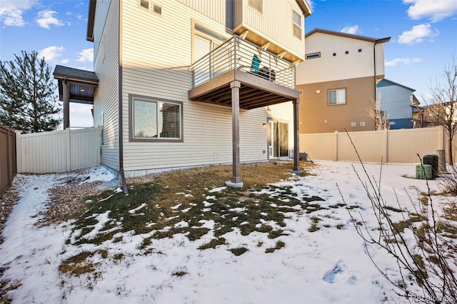 snow covered rear of property featuring a fenced backyard and a balcony