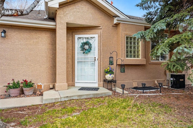 entrance to property featuring stucco siding, central AC unit, and roof with shingles