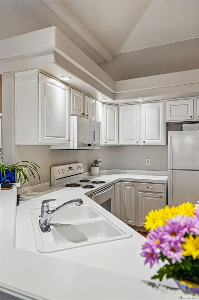 kitchen featuring white appliances, a sink, light countertops, white cabinets, and lofted ceiling