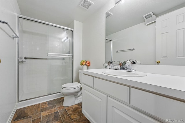 bathroom featuring stone finish floors, toilet, a stall shower, and vanity