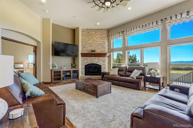 living room with a stone fireplace, hardwood / wood-style floors, a high ceiling, and ceiling fan