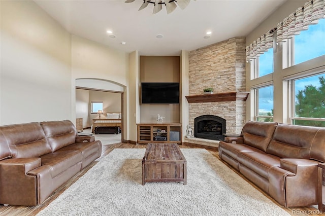 living room featuring a stone fireplace, a high ceiling, light wood-type flooring, and ceiling fan