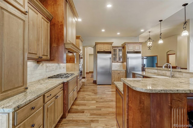 kitchen with backsplash, light wood-type flooring, stainless steel appliances, sink, and decorative light fixtures