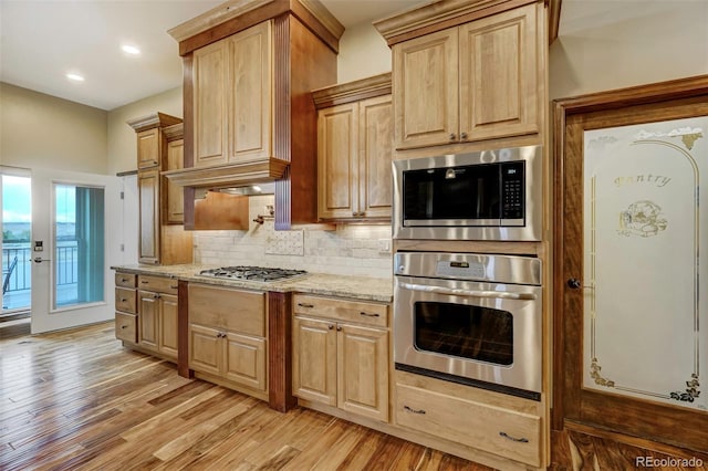 kitchen with light brown cabinets, light stone counters, backsplash, light hardwood / wood-style flooring, and stainless steel appliances