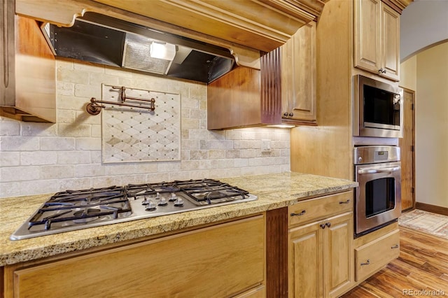 kitchen with backsplash, appliances with stainless steel finishes, light stone countertops, and light wood-type flooring