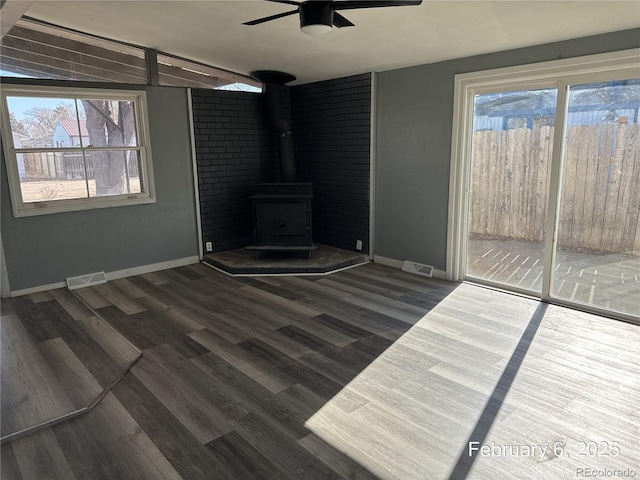 unfurnished living room featuring ceiling fan, a healthy amount of sunlight, dark hardwood / wood-style flooring, and a wood stove