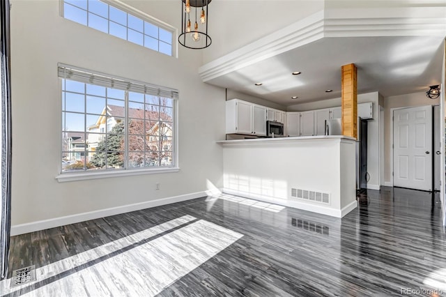 unfurnished living room featuring dark wood-style floors, a healthy amount of sunlight, visible vents, and baseboards