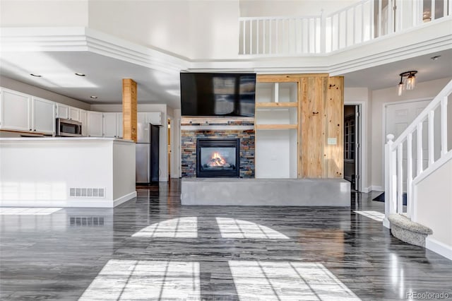 unfurnished living room featuring a high ceiling, a fireplace, visible vents, baseboards, and stairs