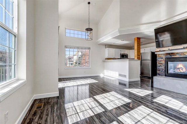 unfurnished living room with high vaulted ceiling, dark wood-style flooring, a fireplace, visible vents, and baseboards