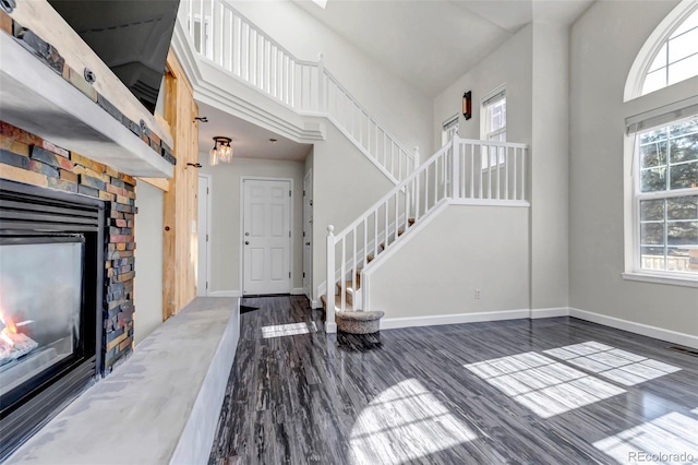 entrance foyer with a high ceiling, baseboards, wood finished floors, and a stone fireplace