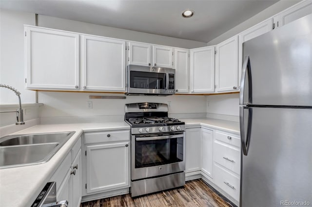 kitchen featuring stainless steel appliances, wood finished floors, a sink, and white cabinetry