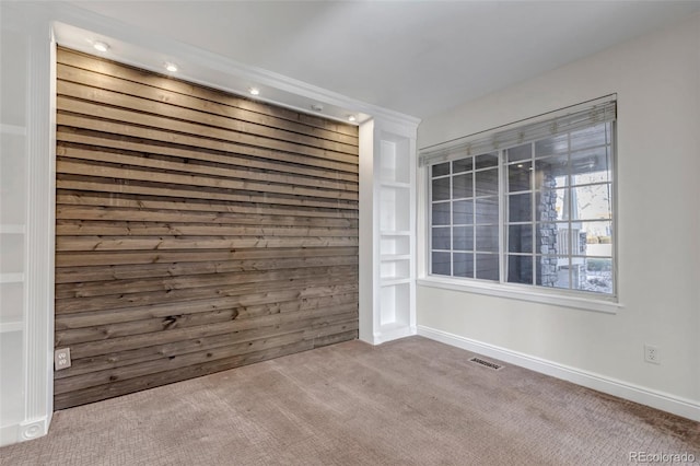 carpeted spare room featuring baseboards, wooden walls, and visible vents