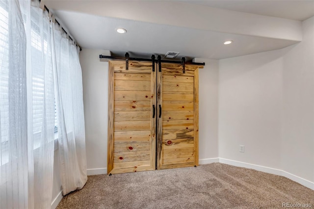 carpeted empty room with recessed lighting, plenty of natural light, baseboards, and a barn door