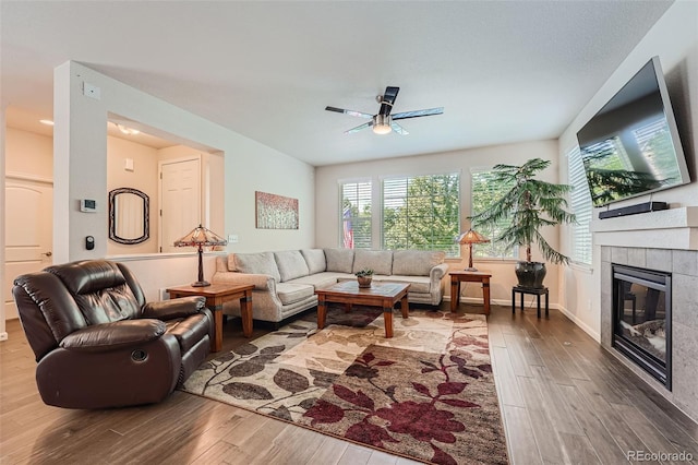 living area with a tiled fireplace, wood finished floors, baseboards, and ceiling fan