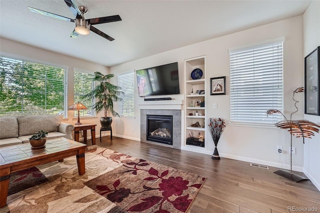 living area featuring built in shelves, a ceiling fan, wood finished floors, visible vents, and a tile fireplace